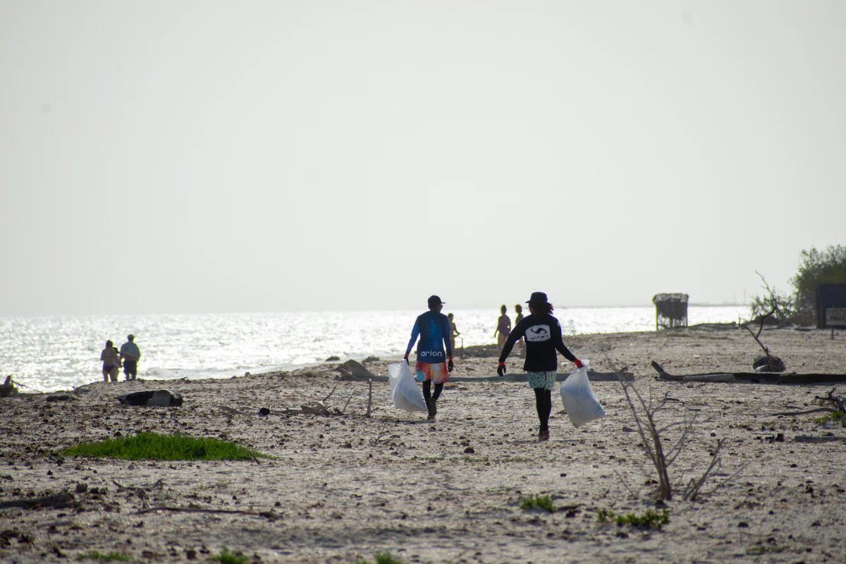 Two volunteers carrying bags of collected waste across the beach