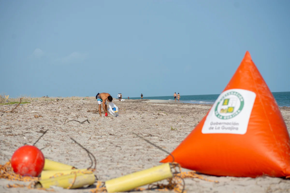 Washed-up buoys and rope on the beach, a person collecting waste in the background