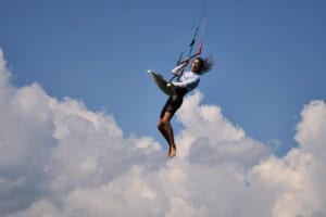 Watersport for Change Instructor Luke Riley zeigt einen hohen Sprung beim Kitesurfen vor blauem Himmel mit Wolken – ein Sinnbild für den Entdeckergeist und das Umweltbewusstsein von OceanPulse.