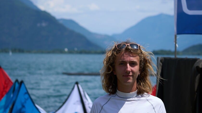 Portrait of Luke Riley, Watersport for Change instructor, standing by the water with kiteboarding kites and mountain scenery in the background.