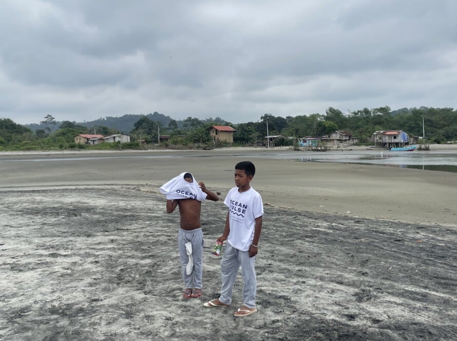 Zwei Jungen am Strand von Mompiche tragen weiße Ocean Pulse T-Shirts nach einer Umweltaktion.