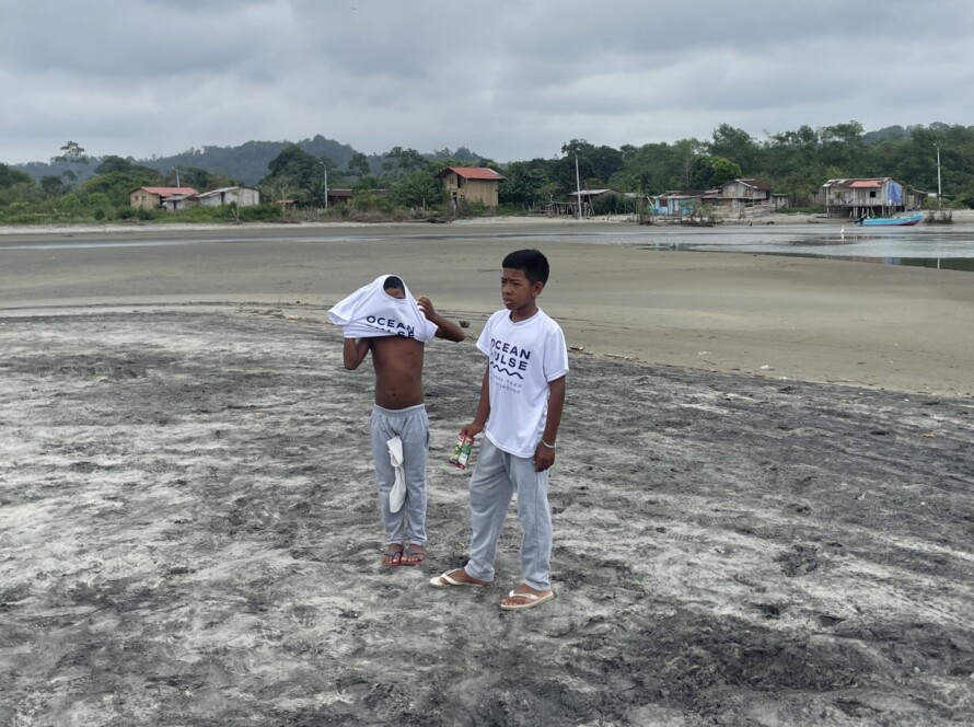 Zwei Jungen am Strand von Mompiche tragen weiße Ocean Pulse T-Shirts nach einer Umweltaktion.