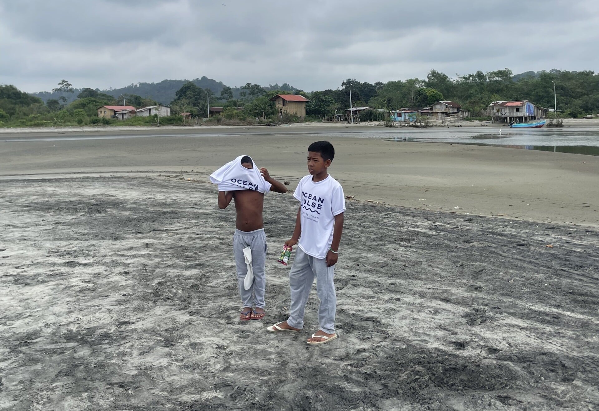 Zwei Jungen am Strand von Mompiche tragen weiße Ocean Pulse T-Shirts nach einer Umweltaktion.